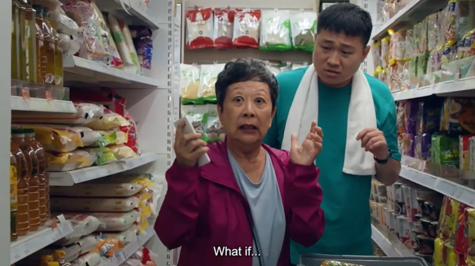 A surprised older woman holding a small white object and a young man in a supermarket aisle.